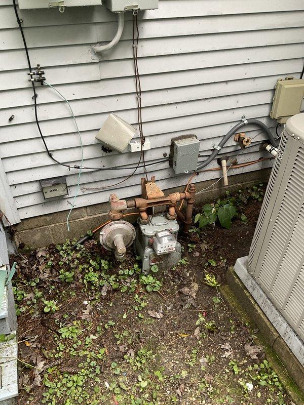Conducted comprehensive site assessment for furnace replacement estimate. Documented existing electrical panel configuration showing dual-column breaker arrangement with main disconnect, verified circuit labeling and panel capacity for new equipment installation. Evaluated exterior utility connections including aged copper gas lines with visible corrosion, existing HVAC equipment placement on concrete pad with vegetation growth, and electrical service routing through exterior junction boxes and conduit. Assessed installation requirements and utility interface points to provide accurate replacement system specifications.
