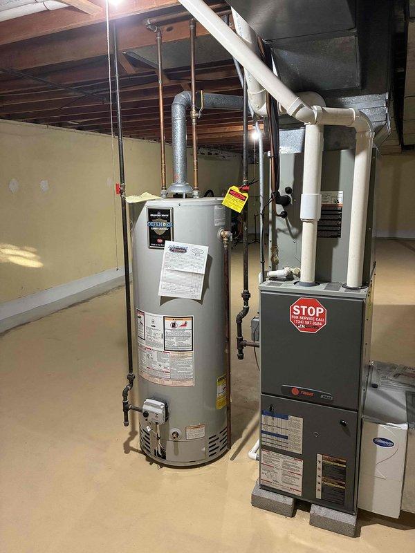 Conducted on-site evaluation of existing HVAC system for complete replacement estimate. Assessed current furnace and air conditioning equipment located in basement utility area, documenting equipment age, condition, and configuration. Photographed existing gray rectangular furnace unit with connected ductwork, cylindrical water heater, and associated piping systems including copper lines and PVC venting. Evaluated mechanical room layout, ceiling clearances with exposed joists, and concrete flooring for equipment access and replacement feasibility. Reviewed furnace specifications and warning labels, noting current installation setup with white PVC exhaust pipes, metal ductwork routing, and humidifier integration. Documented all necessary measurements and equipment specifications to prepare comprehensive replacement proposal for new furnace and air conditioning system.