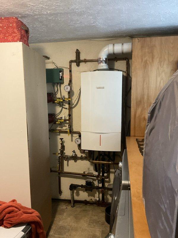 Conducted on-site evaluation of existing Bosch ZWB 42-3 direct-vent propane combi boiler system installed approximately 2015, currently providing both baseboard heating and domestic hot water with no operational issues reported. Documented current installation configuration including copper piping network, dual circulator pumps with expansion loops, multiple isolation valves, pressure gauges, and venting arrangement in basement mechanical room. Photographed complete system layout showing wall-mounted boiler unit, manifold assembly with brass fittings and yellow-handled ball valves, and all associated connections to assess scope of replacement work. Prepared comprehensive estimate for complete system replacement including removal and disposal of existing combi boiler, installation of new high-efficiency combi unit such as Burnham Alta Combi 200K BTU, all necessary materials and components, modifications to existing venting and piping systems as required, reconnection of baseboard heatin