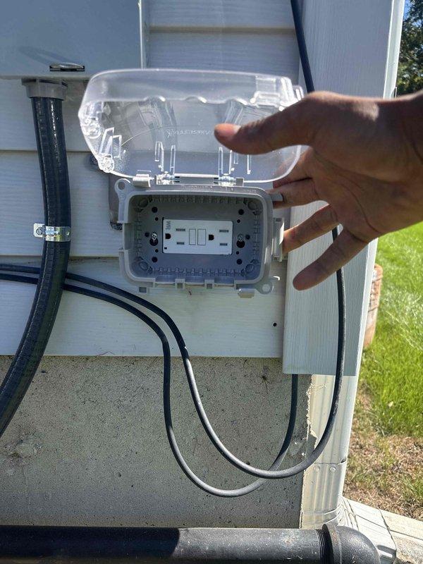 Inspected and documented exterior GFCI outlet installation on residential property. Verified weatherproof cover operation, proper GFCI functionality with test/reset buttons, and secure mounting of outlet box to exterior wall with conduit connections intact.