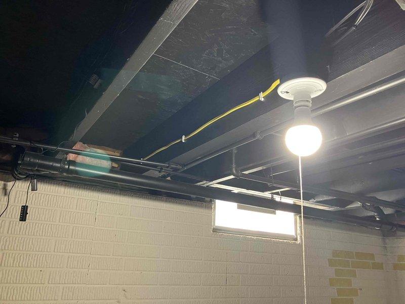 Completed electrical estimate for GFCI outlet installation and basement lighting fixture assessment. Inspected existing outdoor weatherproof GFCI receptacle with Intermatic Type 53R in-use cover mounted on exterior wood siding, confirming proper installation and functionality. Evaluated basement utility area lighting conditions, including ceiling-mounted globe fixture with exposed wiring and conduit routing among floor joists and mechanical systems. Documented electrical infrastructure configuration for estimate preparation.