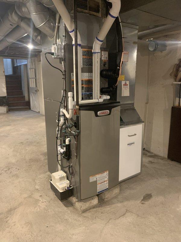 Completed full HVAC system installation in residential basement consisting of 70,000 BTU Lennox furnace and 2-ton air conditioning unit configured for right-side discharge. Installed furnace on concrete pad with proper clearances and connected to existing ductwork system using rigid and flexible metal ducting. Ran yellow gas supply line to furnace with appropriate shutoff valve and made all necessary gas connections per code. Installed condensate drainage piping and connected electrical supply. Mounted AC evaporator coil and completed refrigerant line connections between indoor and outdoor units. Verified all duct connections were properly sealed and secured. Connected humidifier system to water supply and furnace with visible piping along left side of unit. Tested all system operations including heating cycle, cooling cycle, airflow, and safety controls. Confirmed proper ignition sequence, flame characteristics, and temperature rise across heat exchanger. Verified refrigerant charge a