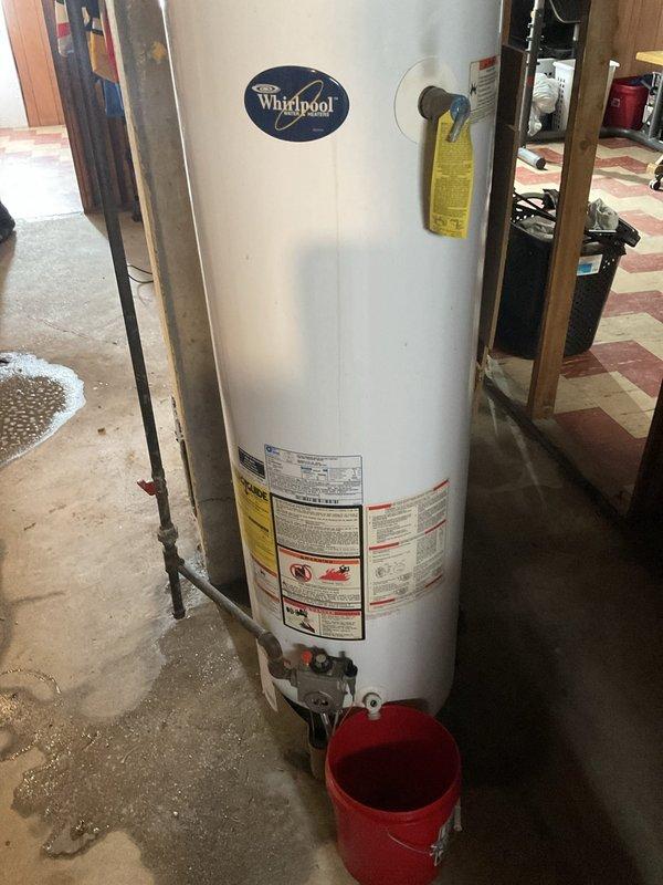 Responded to service call for non-functioning standard water heater with active leak. Upon inspection, confirmed existing Whirlpool unit was leaking and required replacement. Provided estimate for standard water heater replacement in basement utility area. Assessed existing natural draft venting system with metal duct penetrating through ceiling, noting proper sealing with gray sealant material. Documented current installation configuration including gas line connections, plumbing connections, and drainage setup with catch basin in place. Evaluated surrounding framing and floor conditions to ensure proper clearances and support for new unit installation.