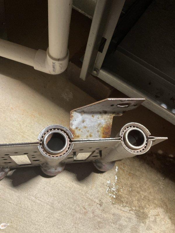 Completed scheduled HVAC maintenance club visit tune-up on residential system during preferred early morning time slot. Performed comprehensive inspection of heating equipment, identifying significant rust and corrosion on gas burner assembly components including burner heads, mounting brackets, and copper tube connections. Documented deteriorated condition of burners showing oxidation, discoloration, and rust deposits throughout metal surfaces and connection points. Removed and photographed corroded burner assembly components for assessment, noting perforated gas distribution ports and aged copper tubing with moisture exposure damage. System components disassembled for thorough cleaning and evaluation of serviceability. Inspected PVC venting and surrounding HVAC equipment access panels. Provided photographic documentation of corroded parts to support maintenance recommendations and future service planning.