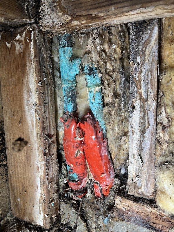 Performed leak detection investigation on a wall cavity with suspected water intrusion. Cut inspection access hole revealing copper pipes with visible T-joint/elbow connections. Documented extensive water damage including deteriorated wooden framing elements, significant mold growth, and moisture-affected insulation. Source of leak appears to be at pipe junction point where severe deterioration was observed.