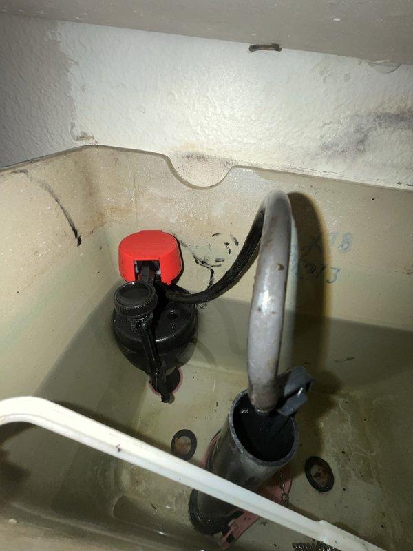 Inspected wall junction and plumbing fixture showing signs of moisture damage. Documented condition of float valve assembly with red cap and adjacent drain pipe. Observed possible mineral deposits or early mold formation on textured surface near pipe conduit.