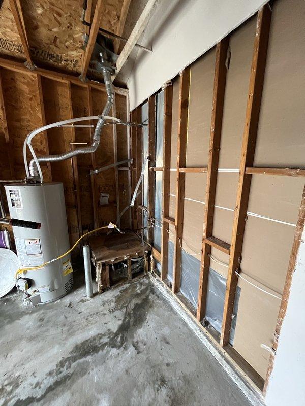 Conducted inspection of basement utility area with visible water damage on concrete floor. Examined unfinished walls with exposed wooden framing and partial insulation to assess potential mold development around water heater and HVAC system. Documented conditions with photographs, noting water stains and possible moisture intrusion requiring remediation to prevent further structural damage and mold growth.