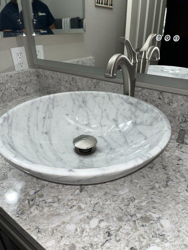 Inspected newly installed vessel-style marble sink and contemporary faucet for proper installation. Verified P-trap connection and drain assembly under sink cabinet, confirming no leaks present in the plumbing system. Documentation photos taken of both the completed fixture installation and underlying plumbing components.