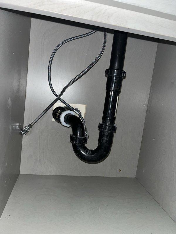 Inspected newly installed vessel-style marble sink and contemporary faucet for proper installation. Verified P-trap connection and drain assembly under sink cabinet, confirming no leaks present in the plumbing system. Documentation photos taken of both the completed fixture installation and underlying plumbing components.
