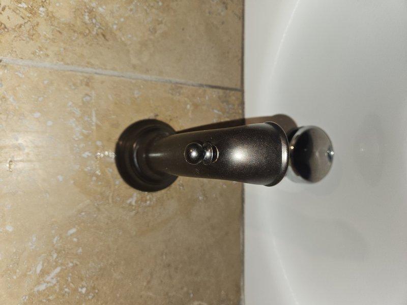 Completed maintenance service on tankless water heater using newly arrived parts. During inspection, accessed wall panel to examine copper plumbing infrastructure behind bathroom wall. Also assessed door stop hardware mounted on textured wall surface for potential adjustment or replacement.