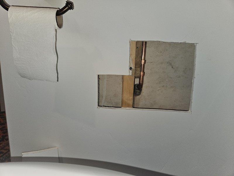 Completed maintenance service on tankless water heater using newly arrived parts. During inspection, accessed wall panel to examine copper plumbing infrastructure behind bathroom wall. Also assessed door stop hardware mounted on textured wall surface for potential adjustment or replacement.