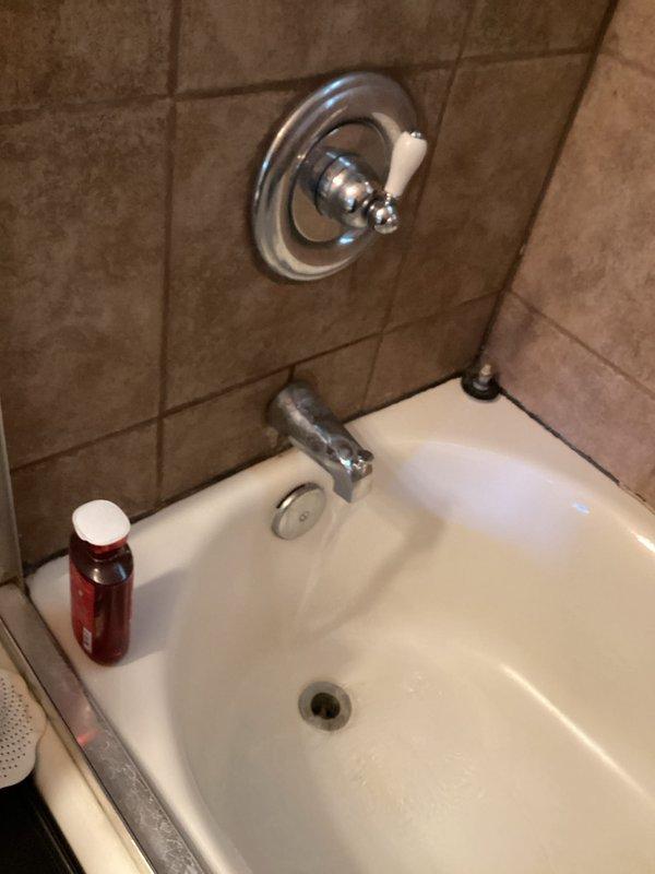 Completed annual plumbing maintenance membership inspection including comprehensive water heater evaluation and flush service. Inspected under-sink drain assembly featuring white PVC tailpiece connected to chrome P-trap with proper wall drain connection, verifying all connections were secure and leak-free. Examined bathroom plumbing fixtures including tub/shower chrome control valve, tub spout, and drain assembly, confirming proper operation and no visible leaks. Water heater inspected and flushed per maintenance protocol; unit is approximately one year old and operating within normal parameters. All plumbing systems found in good working condition with no immediate repairs required.