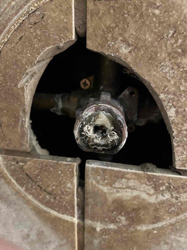 Responded to water leak emergency in main level bathroom where water was dripping from ceiling. Customer had removed ceiling sheetrock and attempted to access shower valve, breaking the cartridge in the process and disabling water flow. Accessed plumbing through floor opening, assessed damaged shower valve cartridge and corrosion on fixtures. Documented conditions via photos showing access point through tile floor and compromised plumbing components requiring cartridge replacement to restore shower function.