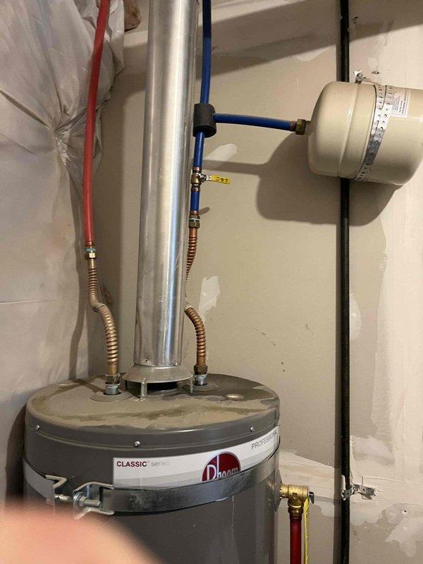 Responded to reported leak from bottom of 8+ year old tanked water heater in basement. Upon inspection, determined unit had reached end of serviceable life with tank failure causing water discharge. Removed and disposed of failed water heater. Installed new Rheem Classic tanked water heater with proper venting through metal flue pipe, connected hot and cold water supply lines using flexible corrugated connectors with brass fittings, and installed expansion tank with blue rigid piping and appropriate mounting. Tested all connections for leaks, verified proper operation, and confirmed system functionality.