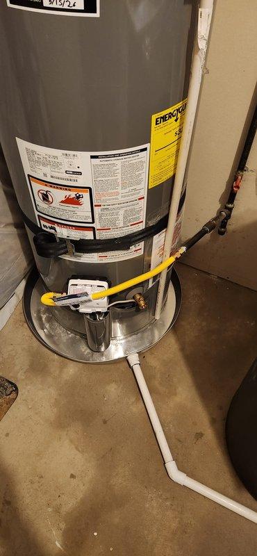 Completed residential water heater installation in basement utility area. Installed new gray cylindrical water heater with proper connections including copper supply lines, yellow flexible gas connectors, PVC condensate drain line with appropriate routing and elbows, and metal drip pan at base. All plumbing connections secured and tested, unit operational and ready for service.