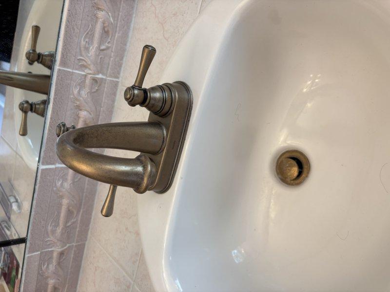 Responded to reported leaks at toilet and bathroom sink. Inspected toilet tank and identified leak originating from bottom of tank, noting significant mineral deposits and corrosion on internal components and tank surfaces. Examined bathroom sink with oil-rubbed bronze fixtures and confirmed leak condition. Documented both fixtures with photographs for assessment and repair recommendations.