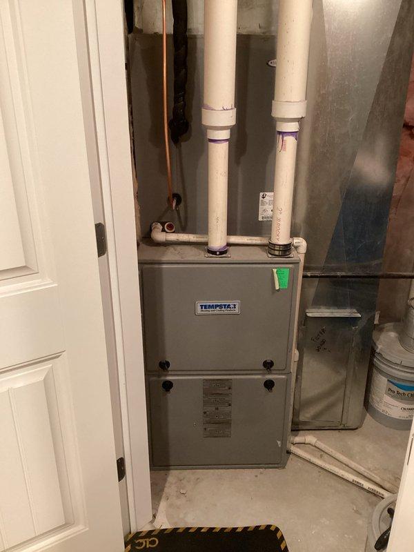 Responded to no-cooling complaint on approximately 10-year-old Tempstar residential forced-air system located in basement utility area. Performed diagnostic evaluation of air handler and associated components. Inspected air filter condition and found moderate dust accumulation on mesh filter media. Examined furnace cabinet, condensate drainage system with PVC piping, and refrigerant line connections. Documented equipment condition through photographic inspection of air handler interior and filter housing assembly.