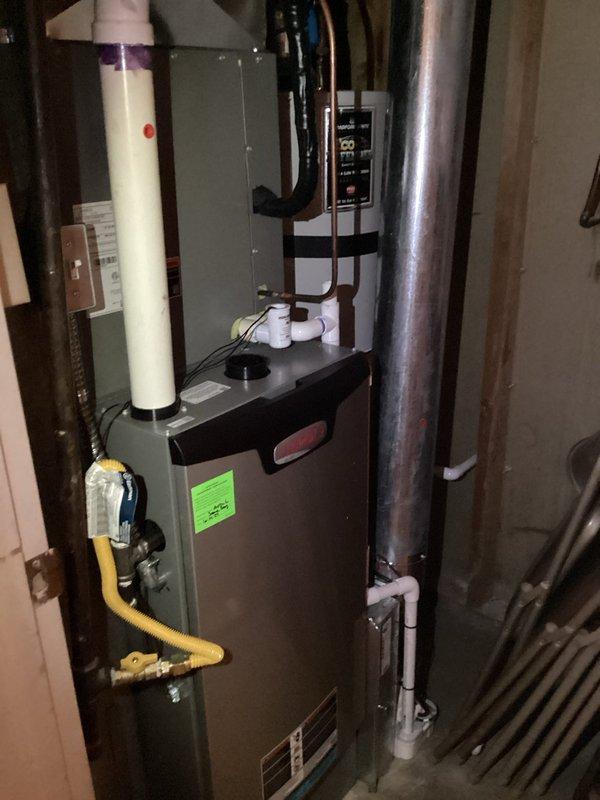 Completed annual air conditioner tune-up on residential split system with outdoor condensing unit and indoor furnace. Performed electrical diagnostics on outdoor unit using clamp meter, measuring amp draw at 48 amps on refrigerant lines and verifying proper electrical operation. Inspected outdoor unit components including copper refrigerant lines with insulation, control wiring, brass service valves, and conduit connections. Evaluated indoor furnace system located in basement, checking gas line connections, PVC vent piping, ductwork, and overall system integration. All equipment operating within normal parameters with no issues identified during maintenance inspection.