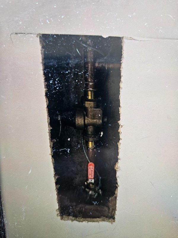 Responded to reported water leak causing saturated flooring in downstairs living room area. Removed section of damaged carpet and underlayment to access subfloor and investigate source of moisture intrusion. Created access opening in wall to expose concealed plumbing system. Located and identified leaking pipe connection in main water supply line. Shut off water supply using main valve to stop active leak and prevent further water damage to flooring and surrounding structure.