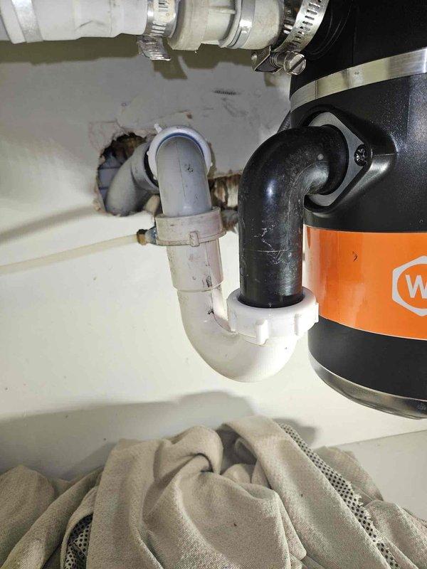 Responded to recurring slow-draining and gurgling kitchen sink that the homeowner suspected was due to inadequate venting following a kitchen remodel. Investigated the drain venting configuration and discussed potential solutions including auto vent installation, explaining that a loop vent or Studer vent was likely already present within the wall cavity. Recommended chemical treatment using Thrift and Total C products rather than mechanical augering to clear the drain line, and provided enzyme-based preventative maintenance cleaner for ongoing use. During the chemical treatment process, the garbage disposal unit began leaking, which was a new issue that had not previously occurred. Immediately notified the homeowner of the disposal leak and documented the condition of the Wolverine brand disposal unit and associated PVC drain assembly with P-trap configuration.