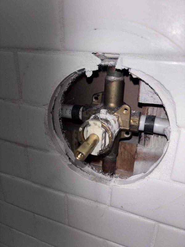 Responded to emergency shower valve failure where handle would not shut off water flow, requiring main water shutoff to the home. Cut access hole through subway tile wall to expose valve assembly mounted on backing board. Replaced defective shower valve cartridge and tested operation to ensure proper water shutoff functionality was restored.