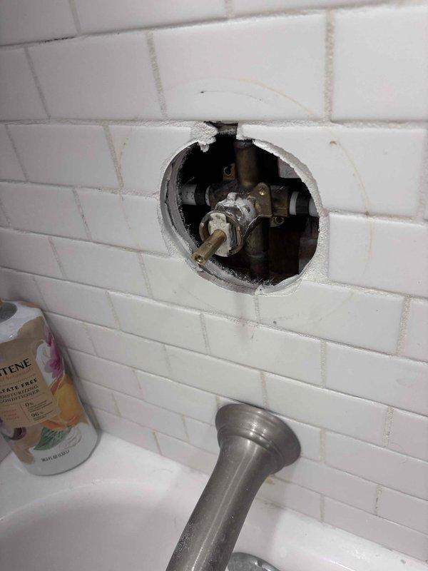 Responded to emergency shower valve failure where handle would not shut off water flow, requiring main water shutoff to the home. Cut access hole through subway tile wall to expose valve assembly mounted on backing board. Replaced defective shower valve cartridge and tested operation to ensure proper water shutoff functionality was restored.