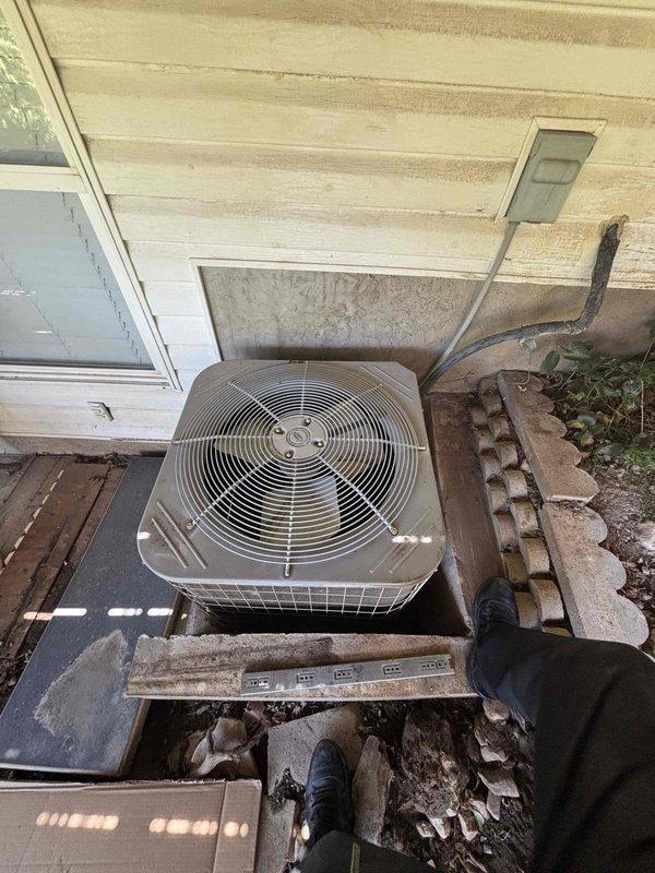 Responded to no cooling complaint on residential single-zone air conditioning system over ten years old with condenser unit located in backyard. Upon arrival, found unit producing warm air at supply vents and condenser making abnormal noises during operation. Performed comprehensive Cool 10+ preventive maintenance inspection including visual assessment of outdoor condenser unit, which revealed aging equipment mounted on deteriorated wooden platform with worn exterior finish. Evaluated refrigerant lines, electrical connections, and overall system operation. Documented equipment condition with photos showing condenser positioning against building exterior, damaged soffit structure above unit, and compromised wooden support base requiring attention for proper equipment stability and drainage.