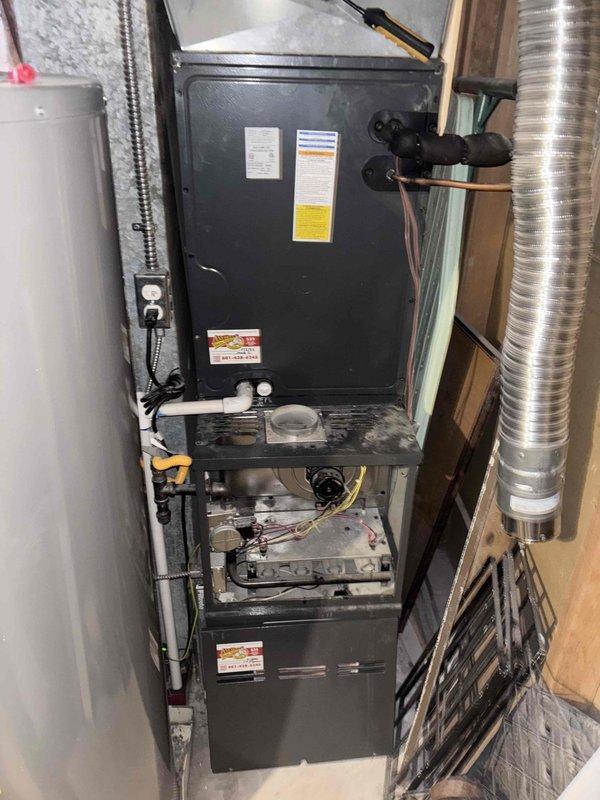 Responded to no-cooling complaint on a two-year-old residential air conditioning system. Performed diagnostic evaluation of the HVAC system located in the basement utility area. Accessed furnace unit and inspected internal components including blower assembly, burner chamber, electrical connections, and associated ductwork. Examined outdoor condensing unit on side of residence. Documented system configuration with furnace positioned adjacent to water heater with flexible metal ductwork and PVC condensate drainage lines. Verified proper access to equipment and photographed installation for service records.