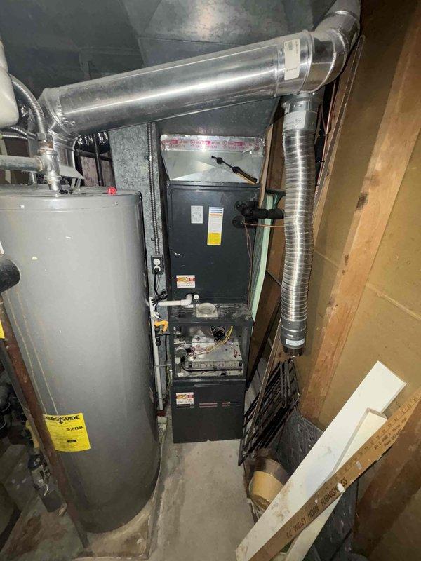Responded to no-cooling complaint on a two-year-old residential air conditioning system. Performed diagnostic evaluation of the HVAC system located in the basement utility area. Accessed furnace unit and inspected internal components including blower assembly, burner chamber, electrical connections, and associated ductwork. Examined outdoor condensing unit on side of residence. Documented system configuration with furnace positioned adjacent to water heater with flexible metal ductwork and PVC condensate drainage lines. Verified proper access to equipment and photographed installation for service records.