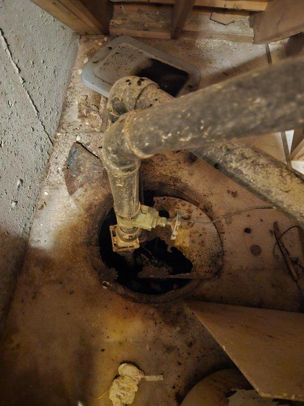 Responded to emergency call for main drain backup affecting main floor bathroom. Upon arrival, inspected basement sewage ejector pump system (approximately 6 years old) and identified significant deterioration and corrosion on pump housing and discharge components. Documented heavily corroded circular pump housing with extensive rust buildup, compromised clear discharge tube with substantial organic accumulation, and overall system failure contributing to drainage issues. Assessed crawl space conditions and photographed failed equipment for documentation and replacement recommendations.