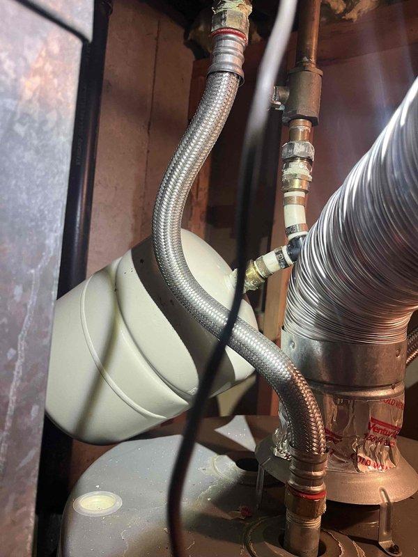 Responded to report of water heater leaking from bottom in basement. Upon arrival, confirmed 9-year-old Rheem tanked water heater with active leak at base of unit. Water supply to unit had been shut off prior to arrival. Inspected unit and determined tank failure due to age and internal corrosion, resulting in water discharge from bottom of tank. Documented condition with photographs showing water heater installation, connected plumbing lines including flexible braided supply hoses with copper fittings, and adjacent HVAC equipment. Advised replacement of failed water heater due to compromised tank integrity.