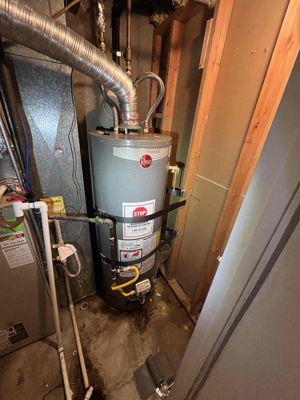 Responded to report of water heater leaking from bottom in basement. Upon arrival, confirmed 9-year-old Rheem tanked water heater with active leak at base of unit. Water supply to unit had been shut off prior to arrival. Inspected unit and determined tank failure due to age and internal corrosion, resulting in water discharge from bottom of tank. Documented condition with photographs showing water heater installation, connected plumbing lines including flexible braided supply hoses with copper fittings, and adjacent HVAC equipment. Advised replacement of failed water heater due to compromised tank integrity.