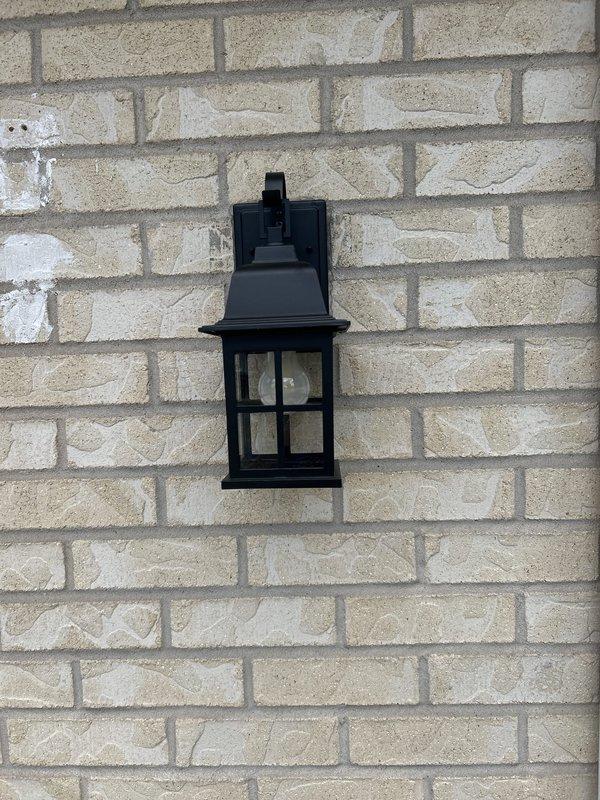 Replaced exterior wall-mounted lantern fixture at front of house on brick and vinyl siding. Removed circuit breaker from electrical panel to safely complete installation. Installed black metal lantern-style fixture with glass panels and verified proper electrical connections and operation.