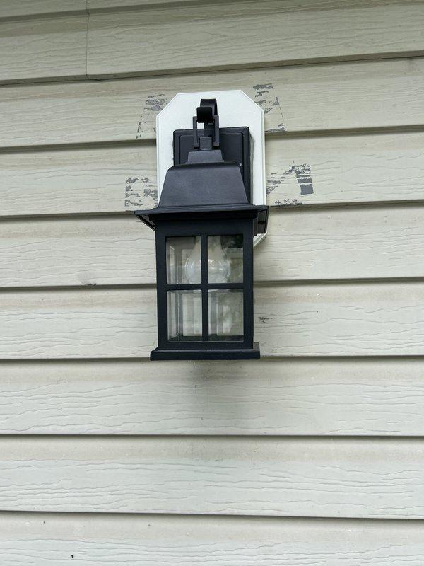 Replaced exterior wall-mounted lantern fixture at front of house on brick and vinyl siding. Removed circuit breaker from electrical panel to safely complete installation. Installed black metal lantern-style fixture with glass panels and verified proper electrical connections and operation.