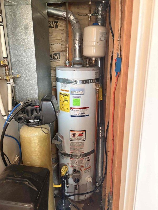 Evaluated residential tank-style water heater installed in 2011 for active leak condition in utility closet. Unit located adjacent to water softener system with expansion tank mounted above and standard venting configuration. Assessed leak source on tank body requiring full replacement due to age and compromised tank integrity. Documented existing installation including copper supply lines, expansion tank, flexible venting, and proximity to HVAC ductwork and water treatment equipment. Provided replacement estimate for new residential water heater with comparable specifications and proper code-compliant installation in existing utility space.