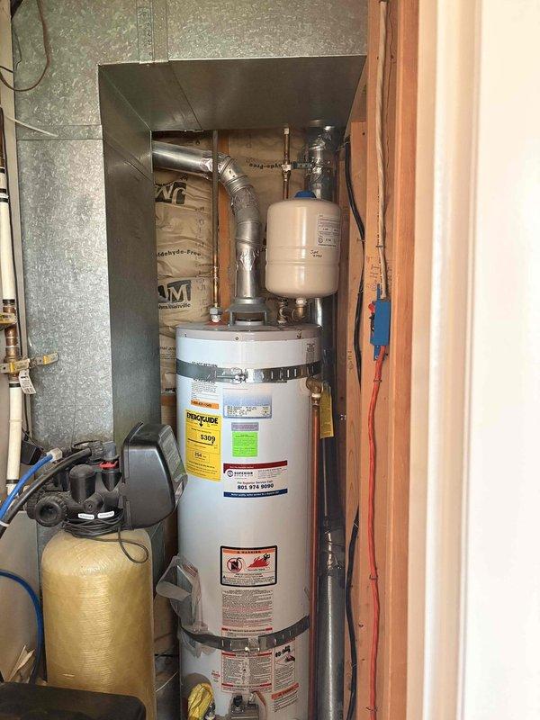 Evaluated residential tank-style water heater installed in 2011 for active leak condition in utility closet. Unit located adjacent to water softener system with expansion tank mounted above and standard venting configuration. Assessed leak source on tank body requiring full replacement due to age and compromised tank integrity. Documented existing installation including copper supply lines, expansion tank, flexible venting, and proximity to HVAC ductwork and water treatment equipment. Provided replacement estimate for new residential water heater with comparable specifications and proper code-compliant installation in existing utility space.