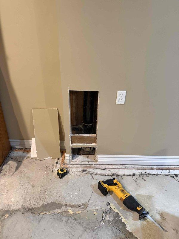 Completed sewer liner installation with wall access point created at floor level to accommodate new piping system. Cut and prepared wall opening, installed black PVC cleanout fitting with circular access port, and staged area for final restoration work including drywall patching and baseboard reinstallation.