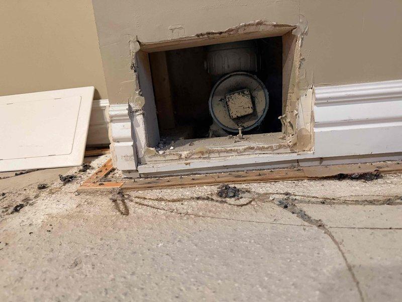 Completed sewer liner installation with wall access point created at floor level to accommodate new piping system. Cut and prepared wall opening, installed black PVC cleanout fitting with circular access port, and staged area for final restoration work including drywall patching and baseboard reinstallation.
