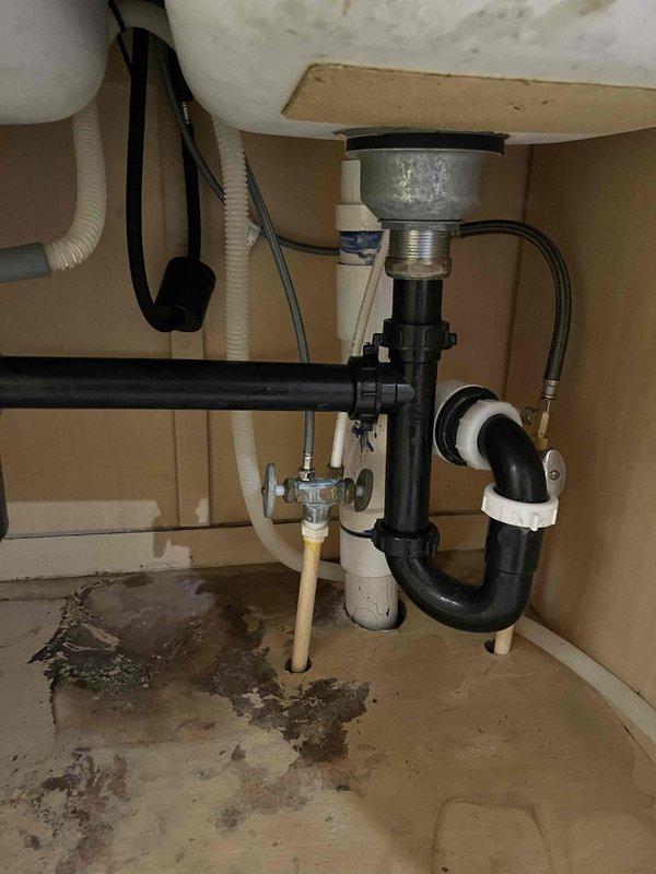 Responded to reported leak under kitchen sink at double basin fixture. Upon inspection, identified active leak in drain assembly and P-trap connection with visible water damage and staining on cabinet floor indicating ongoing moisture intrusion. Assessed plumbing configuration including black plastic drain assembly, P-trap, white PVC drainage connections, braided stainless steel supply lines, and dishwasher drain connection. Provided comprehensive quote for repair of kitchen sink leak and additional basement plumbing installation work including toilet, sink, and shower rough-in. Presented multiple service options including disposal installation with extended warranty coverage.