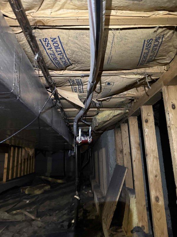 Responded to a no cooling complaint on a single-zone residential HVAC system approximately 7 years old. Inspected outdoor condensing unit located on north side of property and indoor air handling equipment situated in laundry area. Documented system conditions through photographs showing exterior condenser unit on concrete pad with refrigerant lines and basement/crawl space installation with ductwork and insulation. Provided technical assessment and estimate for necessary repairs to restore cooling operation.