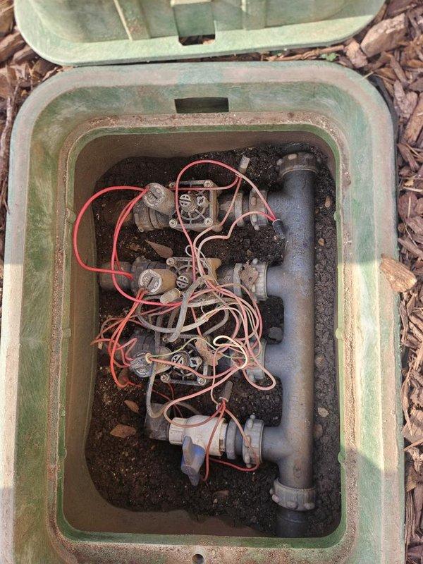Responded to report of water seepage through foundation wall into basement causing carpet damage. Inspected basement plumbing system including copper supply lines with ball valve shut-off at foundation wall area. Investigated exterior irrigation system and located underground valve box containing solenoid valve assembly with multiple zone controls. Determined water intrusion was related to irrigation system malfunction rather than interior plumbing fixture failure. Assessed valve box condition showing signs of weathering, sediment accumulation, and potential valve leakage contributing to moisture migration toward foundation. Recommended irrigation system repairs to address seepage issue and prevent further water damage to basement area.