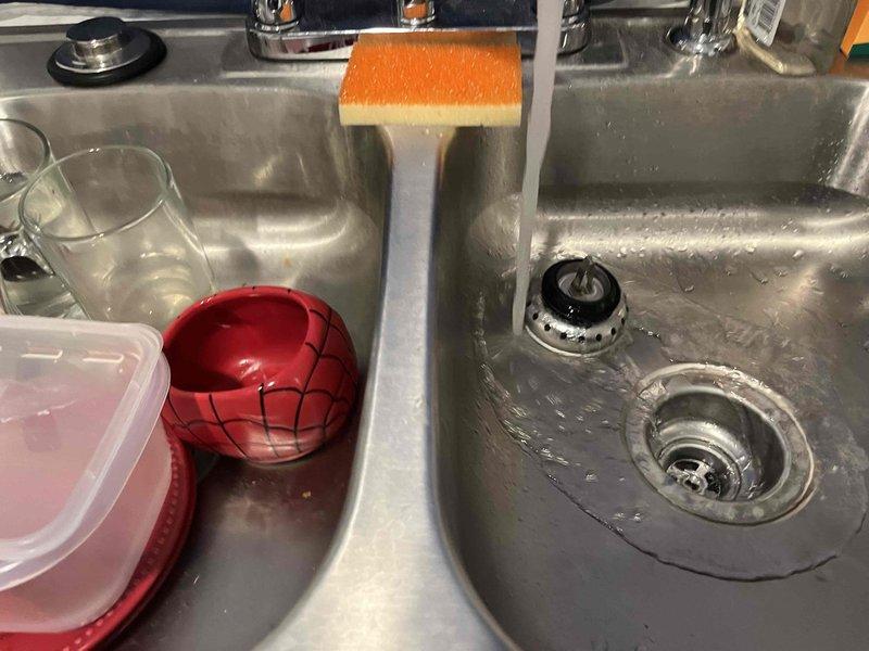 Responded to kitchen sink drainage issue in double-basin stainless steel sink where one basin was overflowing when the other was filled. Assessed drain assemblies and piping configuration in recently remodeled kitchen with no garbage disposal present. Inspected drain strainers, stoppers, and tailpiece connections to identify blockage or improper venting causing backup between basins, and performed necessary repairs to restore proper drainage function.
