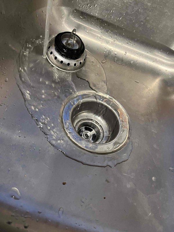 Responded to kitchen sink drainage issue in double-basin stainless steel sink where one basin was overflowing when the other was filled. Assessed drain assemblies and piping configuration in recently remodeled kitchen with no garbage disposal present. Inspected drain strainers, stoppers, and tailpiece connections to identify blockage or improper venting causing backup between basins, and performed necessary repairs to restore proper drainage function.