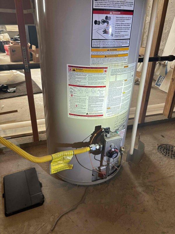 Responded to no hot water complaint on 25+ year old tanked water heater in basement. Upon inspection, diagnosed failed gas valve on unit that had exceeded its expected service life. Documented existing installation with yellow flexible gas line connection and current gas control assembly condition. Recommended full water heater replacement due to age and component failure.