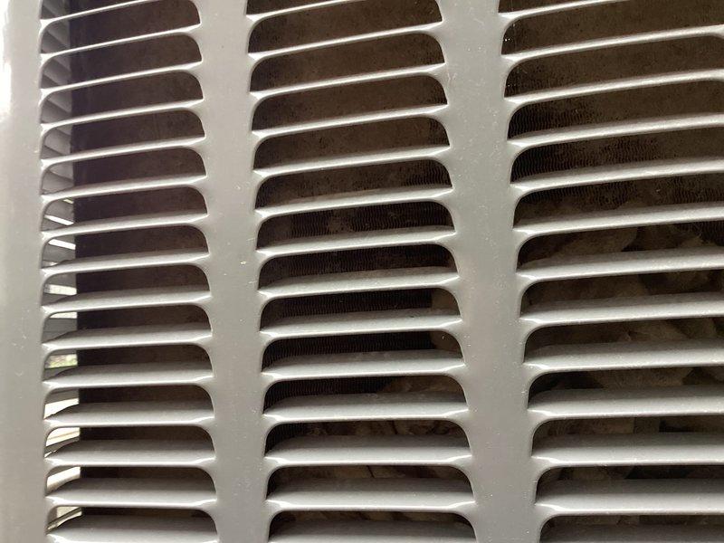 Responded to report of wheezing system and improperly mounted filter on 5-year-old single-zone HVAC system with ground-mounted condenser and basement furnace. Inspected return air grille showing dust accumulation on louvered slats and verified outdoor condenser unit condition on cracked concrete pad. Corrected air filter installation and addressed airflow restriction causing abnormal system noise.