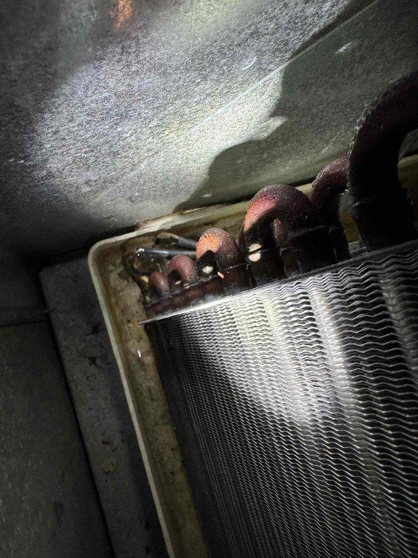 Responded to service call for AC system that would not shut off and was unable to cool below mid-70s. Customer reported water accumulation near unit and debris found in coolant valve. Upon arrival, located 10-year-old AC system and 4-year-old furnace unit. Performed comprehensive Cool 10+ preventive maintenance inspection on system. Inspected evaporator coil assembly and found heat exchanger with aluminum fins in serviceable condition. Examined copper refrigerant line connections showing age-related oxidation and corrosion. Noted moisture staining and condensation patterns in air handler enclosure indicating previous water exposure. Checked all refrigerant lines and connections for integrity. Evaluated thermostat function related to reported continuous operation issue. Documented equipment condition with photographic evidence of coil assembly and heat exchanger components. System inspected for proper drainage and debris accumulation in condensate system.