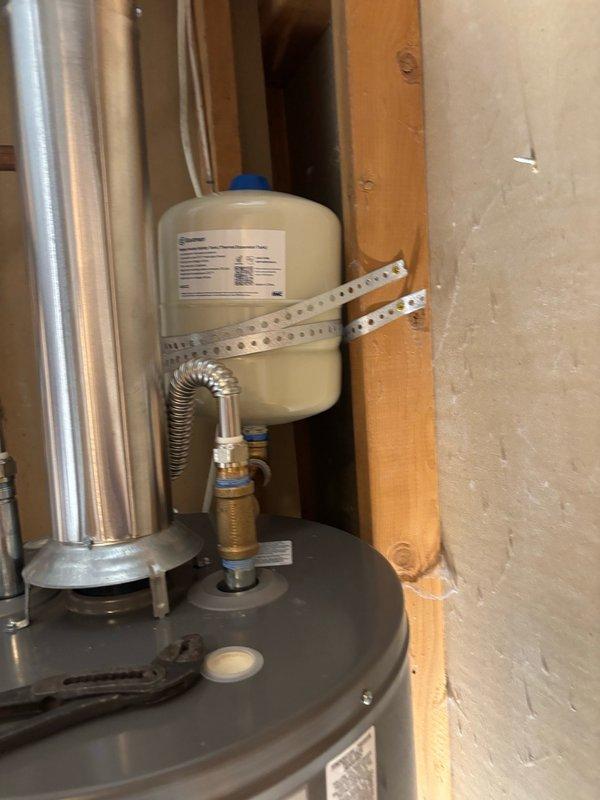 Completed water heater installation in residential utility space. Installed new gray tank water heater with proper connections including copper supply lines and flexible corrugated stainless steel connectors. Mounted white expansion tank to wall framing using metal perforated strapping and secured to wooden studs. Connected all hot and cold water supply lines with appropriate brass fittings and valves. Verified all plumbing connections for proper sealing and tested system operation. Installation completed per code requirements with all components properly secured and functional.