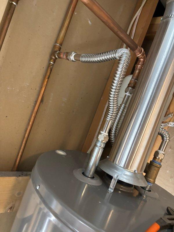 Completed water heater installation in residential utility space. Installed new gray tank water heater with proper connections including copper supply lines and flexible corrugated stainless steel connectors. Mounted white expansion tank to wall framing using metal perforated strapping and secured to wooden studs. Connected all hot and cold water supply lines with appropriate brass fittings and valves. Verified all plumbing connections for proper sealing and tested system operation. Installation completed per code requirements with all components properly secured and functional.