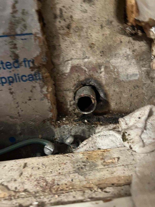 Responded to basement leak investigation. Upon inspection, identified heavily corroded copper pipe fitting beneath sink fixture with significant green oxidation and mineral deposits, causing active leak. Corroded connection showed advanced deterioration with failed yellow foam sealant around pipe penetration through cabinet base. Documented water damage to surrounding wooden surfaces and accumulation of moisture-related staining on adjacent plumbing components.