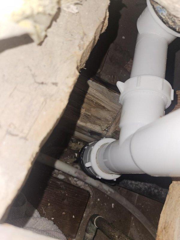 Responded to reported leak at bathroom tub shower drain with easy access. Inspected underfloor plumbing assembly consisting of white PVC drainage pipes and fittings installed between floor joists, noting signs of age and weathering on surrounding wooden structural elements. Evaluated brass supply piping, valves, and galvanized steel connections mounted to concrete block wall in utility area. Documented existing plumbing configuration and leak location with photographic evidence for service records.
